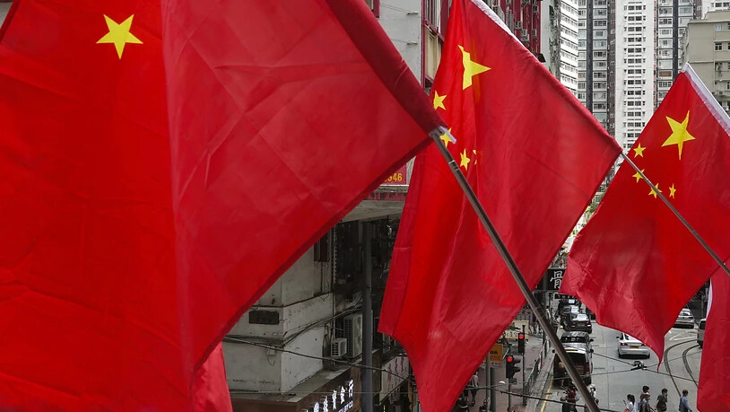 Menschen laufen unter chinesischen Flaggen, die als Teil einer Flaggenzeremonie aufgestellt wurden. Foto: Vincent Yu/AP/dpa/Symbolbild